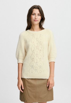 Cream-colored knit sweater with short puff sleeves, featuring a textured diamond pattern and ribbed hem. Paired with a brown leather skirt.