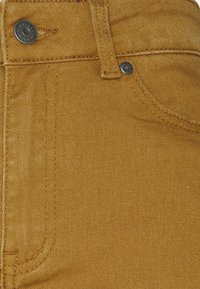 Schmale Jeans in senfgelbem Denim, ausgestattet mit klassischem Fünf-Taschen-Design, Metallnieten und sichtbarem Steppnaht-Muster.