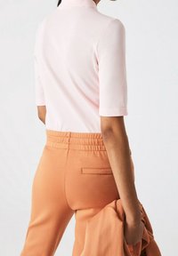 Růžový krátký rukáv s límečkem, spárovaný s pomerančovými kalhotami s elastickým pasem. Halenka má texturovanou látku; kalhoty mají detail zadní kapsy.