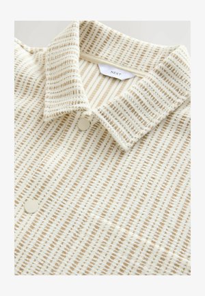 Camicia a righe crema e beige con colletto classico, realizzata in tessuto texturizzato, con chiusura a due bottoni e sottili motivi su tutta la superficie.