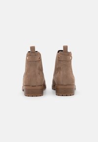 Par de botas de tobillo de ante topo con tacones apilados y tiradores, vistas desde la parte de atrás sobre un fondo blanco.