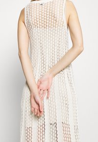 Ärmelloses Strickkleid in Off-White mit detailliertem Spitzenmuster und vertikalem Streifendekor, mit offenem Rücken und lockerer Passform.