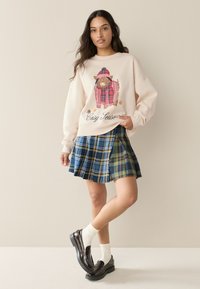Sudadera rosa claro con un diseño de oveja de dibujos animados y el texto "Cosy Season", combinada con una falda plisada de cuadros azul y zapatos negros brillantes.