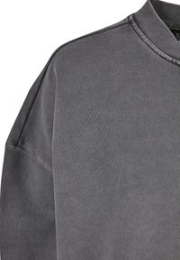 Sweat-shirt gris foncé à col rond avec col côtelé et coutures apparentes sur l'épaule et la manche.