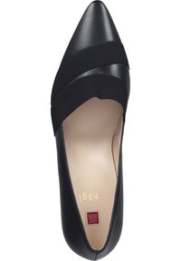 Scarpa nera con punta a punta, realizzata in pelle, con bande elastiche sulla parte anteriore, interno beige e una decorazione quadrata rossa vicino al tallone.
