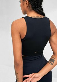 Top court noir à côtes avec un design ajusté, doté de bretelles larges et d'un petit logo en argent accentuant l'ourlet, associé à un legging coordonné.