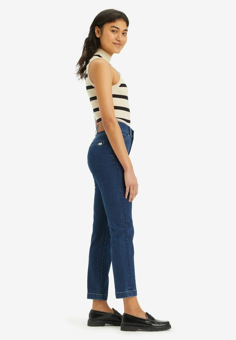 Top sans manches rayé en crème et noir, jean bleu taille haute, et mocassins noirs. Les jeans ont une jambe droite et un ourlet retroussé.
