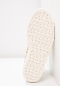 Semelle de sneaker rose clair avec une surface en caoutchouc blanc texturé, arborant un motif géométrique et un petit logo.