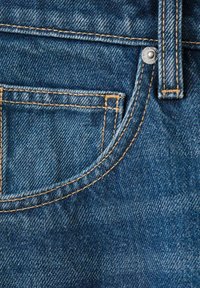 Poche de jean en denim bleu avec des coutures orange, un rivet métallique et une boucle de ceinture en gros plan.
