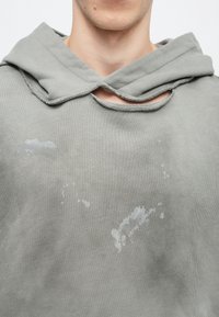 Γκρι φούτερ με κουκούλα, που διαθέτει μοναδικό λάκκο στον λαιμό, ελαφριά λεκέδακια επένδυσης και απαλό υλικό.