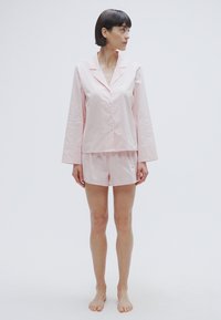Haut de pyjama rose clair à manches longues avec un col cranté, accompagné d'un short assorti. Les deux sont en tissu lisse et présentent une coupe décontractée.