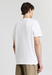T-shirt bianca a maniche corte con un motivo a maglia testurizzata, caratterizzata da un collo rotondo e orlo diritto, abbinata a pantaloni beige chiaro.