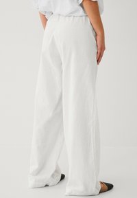 Pantaloni ampi bianchi in lino con vita alta, caratterizzati da una vestibilità rilassata e una texture sottile, abbinati a décolleté nere a punta.