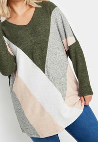 Pull vert surdimensionné avec un décolleté en V, des manches longues, et un design en blocs de couleurs avec des sections grises, roses et blanches. Tissu doux et texturé.