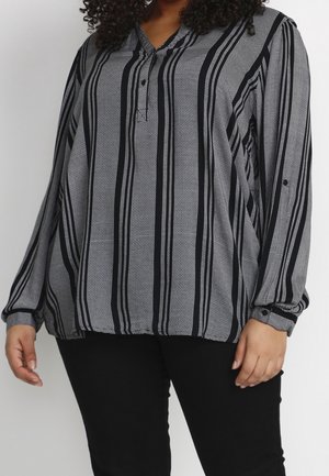 Kvinde iført en sort- og hvid vertically striped langærmet bluse med knappede manchetter og sorte bukser.