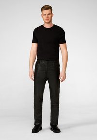 Schwarze Lederhosen mit schmaler Passform und glatter Textur, Vorderknopfverschluss und seitlichen Taschen, kombiniert mit einem enganliegenden schwarzen T-Shirt.