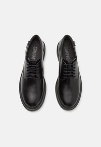 Paire de chaussures en cuir noir à lacets, bouts arrondis et semelles épaisses, vues de dessus sur un fond blanc uni.