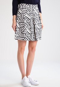 Black and white pleated skirt with geometric pattern and contrasting stripes, made from lightweight fabric. Worn with white sneakers.