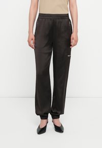 Black satin jogger pants with an elastic waistband, featuring zippered pockets and ribbed cuffs, paired with black slip-on shoes.