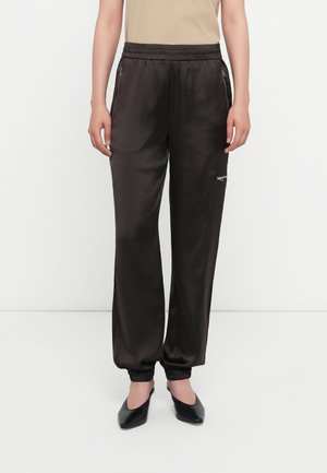 Sorte sateng joggerbukser med elastisk midje, med glidelåslommer og ribbestrikkede mansjetter, sammen med sorte slip-on sko.