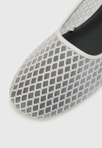 Scarpa intrecciata grigia chiara con motivo a rombi, interno nero e finitura bianca attorno all'apertura. La superficie texturizzata aggiunge dettaglio.