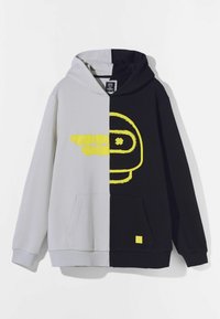 Hoodie med delad design: ljusgrå på ena sidan, svart på den andra, med gula grafiker och en framficka.