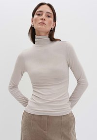 Beige Ripp-Turtleneck-Oberteil mit langen Ärmeln, taillierter Passform, weicher Textur und hohem Kragen. Kombiniert mit einem strukturierten Cordrock.