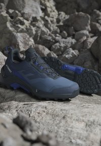 Blå och svarta träningsskor med en texturerad överdel, gummigreppsåle och förstärkt tå. Har djärva svarta ränder på sidorna.