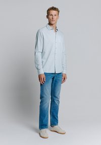 Chemise à manches longues bleu clair à motifs avec des boutons, assortie à un jean bleu clair et des baskets de couleur claire. Design simple et moderne.
