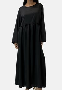 Abito nero a maniche lunghe realizzato in tessuto liscio, con una vestibilità rilassata, vita arricciata e gonna fluente. Scollo rotondo e lunghezza fino alla caviglia.