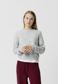 Pull en tricot gris clair avec un col rond et des manches longues, associé à un pantalon rayé rouge et bleu marine avec une taille élastique.
