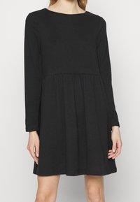 Schwarzes langärmliges Kleid mit rundem Ausschnitt, tailliertem Oberteil und ausgestelltem Rock, aus weichem Stoff mit glatter Textur.