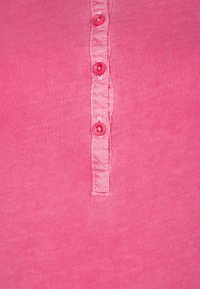 Top in cotone rosa con apertura a bottoni a cinque bottoni, texture liscia e design a coste, che indica uno stile casual.