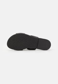 Svart sandal med en texturerad gummisula som har ett präglat mönster och en slät fotbädd. Justerbar rem för en säker passform.