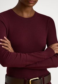 Burgundi színű kötött hosszú ujjú felső kerek nyakkivágással és bordázott mandzsettával, barna övvel párosítva, amely arany csatdíszes.