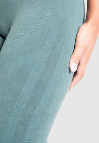 Leggings turchesi con una finitura testurizzata presentano strisce verticali e un tessuto liscio. La vista ravvicinata evidenzia la forma e la vestibilità attorno alla coscia.