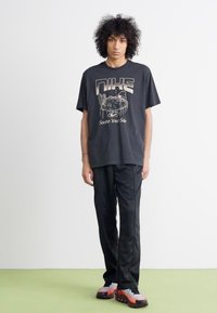 Sort Nike t-shirt med grafisk design og tekst, parret med sorte bukser og multicolore sneakers med røde og grå accenter.