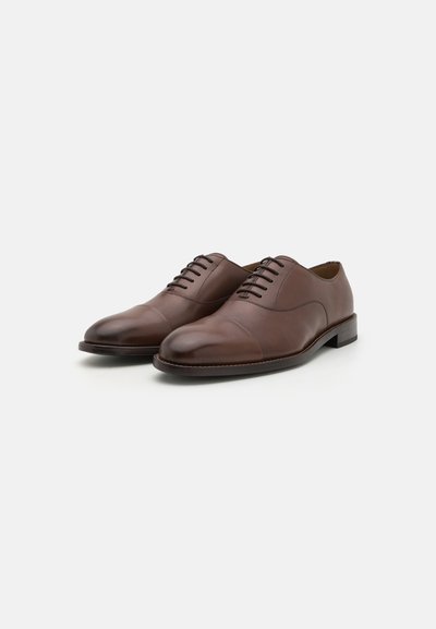 Chaussures de cérémonie en cuir marron avec un bout arrondi, une texture lisse, des détails gaufrés et cinq œillets pour les lacets, avec un petit talon empilé.