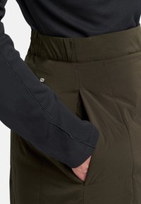 Gekwiltde olijfgroene rok met een hoge elastische tailleband, voorzien van zijzakken en een gestructureerd zwart shirt met lange mouwen.