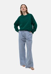 Sweatshirt en coton vert avec des épaules tombantes associé à un pantalon large rayé bleu clair. Les deux pièces ont une coupe décontractée et une texture douce.