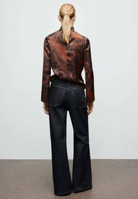 Top de manga larga con patrón de cachemira marrón, combinado con pantalones anchos de mezclilla oscura. Tela suave, ajuste estructurado, detalles de costura visibles.