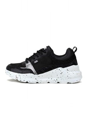 Sneaker nera con pannelli testurizzati, dotata di una tomaia in pelle liscia, suola bianca macchiata e lacci neri. Accentuata da un logo argentato.