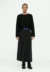 Top negro de manga larga y falda de denim negro con una abertura frontal. Combinado con un cinturón de denim azul y botines negros. Textura suave, diseño minimalista.