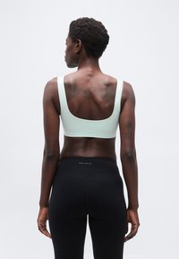 Γυναίκα με κοντά σγουρά μαλλιά που κοιτάζει προς τα πίσω, φορώντας λευκό αθλητικό σουτιέν και μαύρο κολάν, με τατουάζ στην πάνω πλάτη και τα χέρια.