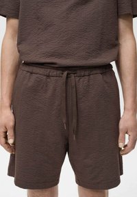 Shorts en tricot brun texturé avec taille élastique et cordon de serrage. Le tissu présente un motif en grille subtil et un design à coupe décontractée.