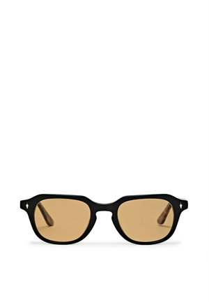 Monture de lunettes rectangulaire noire avec des verres teintés ambre reposant sur une surface blanche.