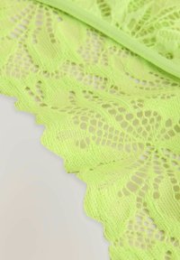 Helles limonengrünes Spitzenmaterial mit einer gewellten Kante, das ein kompliziertes Musterschema und eine strukturierte offene Webart zeigt.