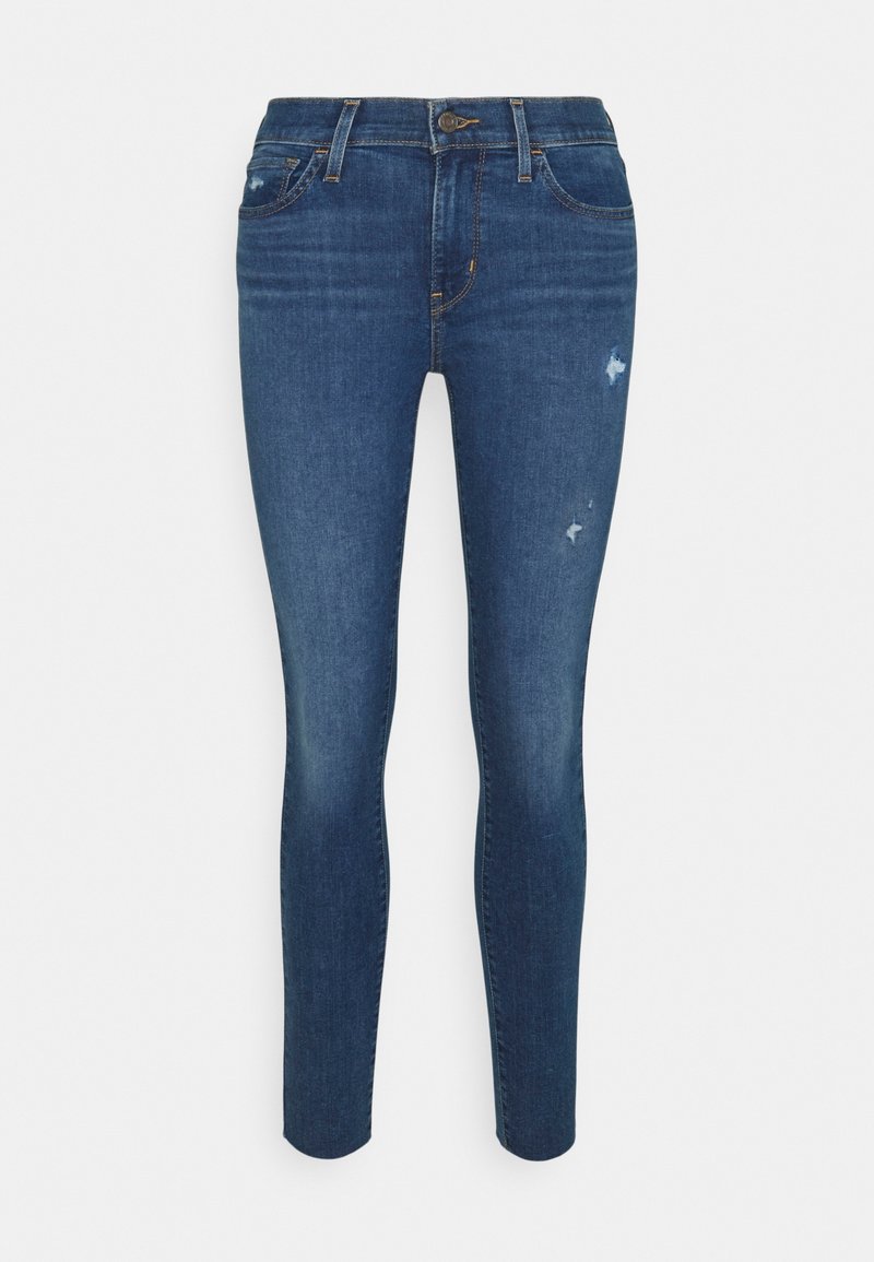 Jean skinny bleu foncé avec légère usure sur la cuisse droite, poches avant, passants de ceinture et fermeture par bouton.