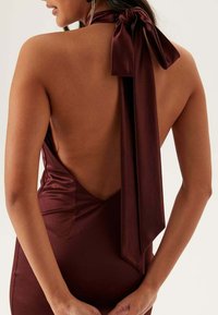 Baksidan av en burgundy sidenklänning med djup V-ringning, halterneck med en stor rosett och slät, figurnära textur.