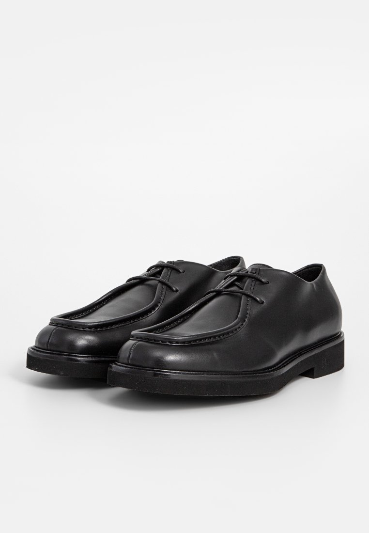 Par de zapatos de vestir de cuero negro con cordones, con puntas cuadradas redondeadas y suelas gruesas sobre fondo blanco.